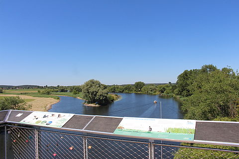 Zwei Informationstafeln am Geländer der Aussichtsplattform in Premnitz. Dahinter der Fluss Havel. Der Himmel ist strahlend blau.