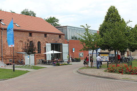 Lilielthalcentrum in Stölln. Ein großes Gebäude aus roten Backsteinen. Davor ein geplsterter Platz mit Bäumen.