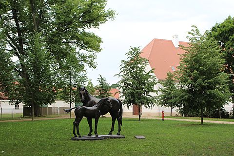 Denkmal aus Bronze bestehend aus einer Stute mit Fohlen umgeben von altem Bäumen.